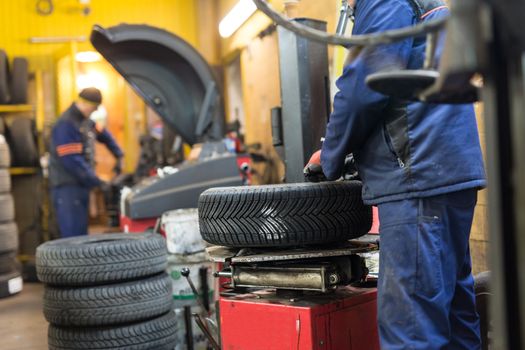 Professional auto mechanic replacing tire on wheel in car repair workshop.