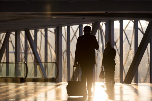 Businessman dragging a small carry on luggage suitcase at airport corridor walking to departure gates.