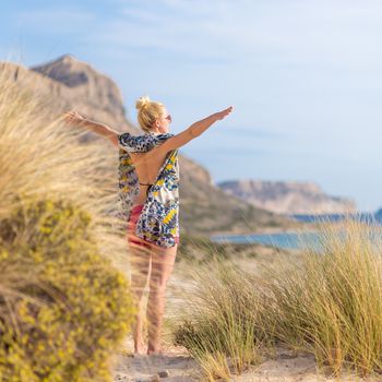 Relaxed woman wearing colorful scarf, enjoying sun, freedom and life at beautiful Balos beach in Greece. Concept of holidays, vacations, freedom, joy and well being.