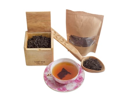 Saucer and cup of black tea, different varieties of tea leaves in paper bag, wooden box and wooden spoon on a light background
