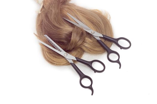 Normal hairdressers scissors and thinning shears against the backdrop of strand of female hair on a light background. 
