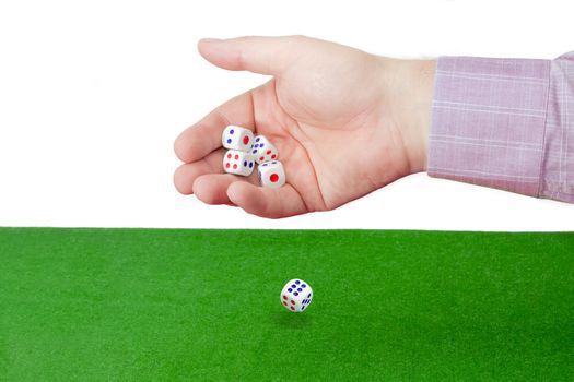 Traditional plastic white six-sided dice with red and blue dots thrown from a male hand on the table with green cloth on a light background. Four dice still in hand, one in the fall.
