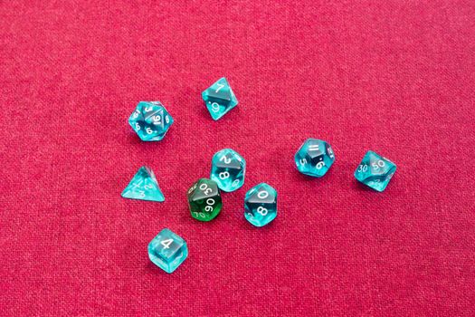 Set of blue and green specialized polyhedral dice with numbers used in role-playing games on a table with red cloth
