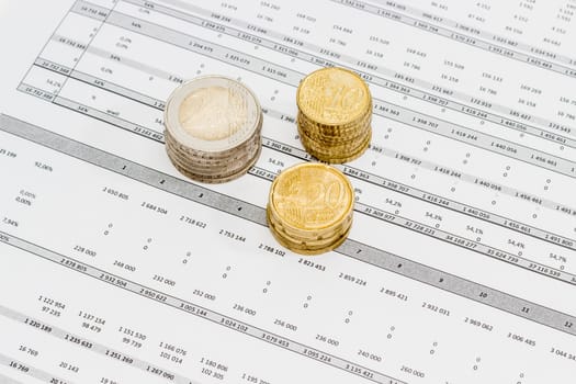 Several euro coins from 10 cents to 2 euro stacked on the printed table with data
