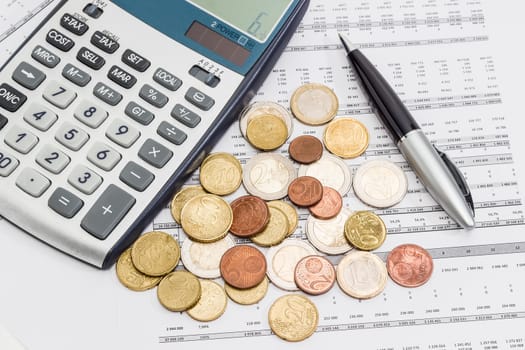 Several euro coins from 1 cents to 2 euro scattered on the printed table with data, pen and fragment of a calculator 
