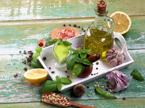 Arrangement of Freshly Made Creamy Pesto Sauce in Glass Gravy Boat with Raw Ingredients and Olive Oil in White Wooden Tray on Cracked Wooden background
