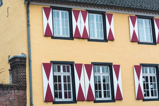 Facade of the county museum Zons in Germany on the Rhine. House front with red and white window shutters.