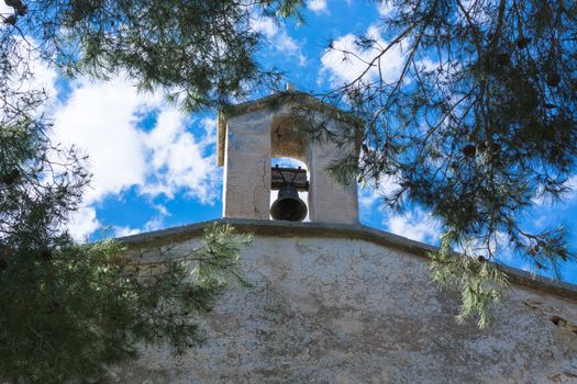 Church tower with bell in Spanish style against a blue sky.