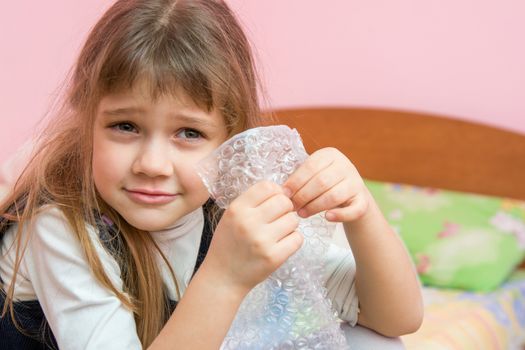 Five-year girl listens to burst like bubbles on the packaging bag