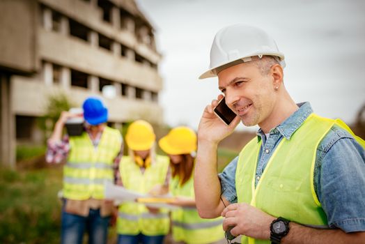 Construction architects using phone in front building damaged in the disaster.