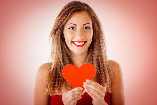 Beautiful smiling girl holding a red heart. Looking at camera.