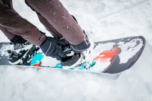 Close-up of man hands adjusting bindings on snowboard boot.