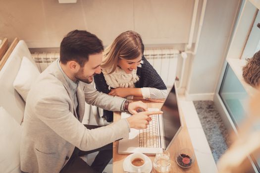 Two beautiful smiling businesspeople working on laptop on a break at cafe. Top view.