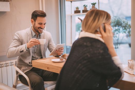 Young smiling businesspeople on a break in a cafe. Man working at tablet and drinking coffe. Woman using smart phone. Selective focus. Focus on businessman.