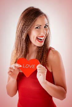 Beautiful smiling girl holding a red heart that says Love. Looking at camera.