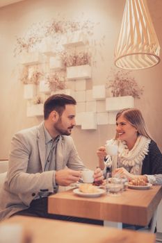 Young man and young woman sitting at cafe and talking with smile. They drinking coffee and having breakfast.