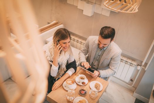 Young smiling businesspeople sitting at cafe and working. They drinking coffee and having breakfast. Top view.