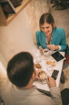Young man and young woman sitting at cafe and talking with smile. They drinking coffee and having breakfast. Selective focus. Focus on businesswoman. Top view.