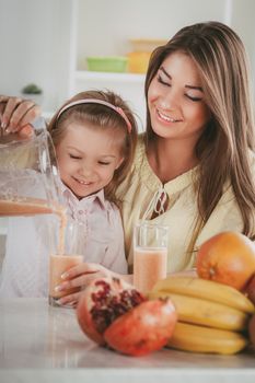 Mother and daughter preparing healthy fruit drink or meal in a blender in the kitchen. 