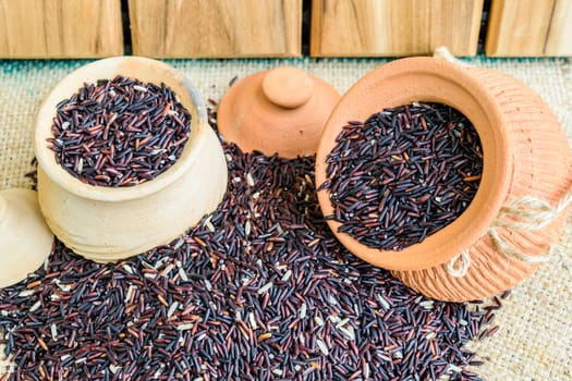 Hom Nil (black jasmine rice) in clay pot on sack wooden background