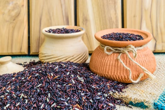 Hom Nil (black jasmine rice) in clay pot on sack wooden background