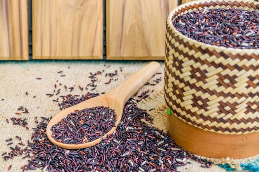 Hom Nil (black jasmine rice) in kratip and wooden spoon on sack wooden background