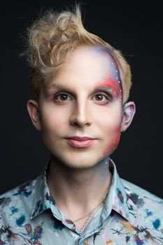 Portrait of beautiful young man with modern hairstyle, artistic multicolor makeup and rhinestones on the face. Studio shot. Black background