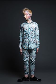 Portrait of beautiful young man with modern hairstyle, artistic multicolor makeup and rhinestones on the face. Studio shot. Black background