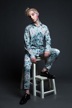 Portrait of beautiful young man with modern hairstyle, artistic multicolor makeup and rhinestones on the face. Studio shot. Black background