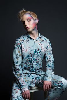 Portrait of beautiful young man with modern hairstyle, artistic multicolor makeup and rhinestones on the face. Studio shot. Black background