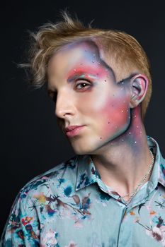 Portrait of beautiful young man with modern hairstyle, artistic multicolor makeup and rhinestones on the face. Studio shot. Black background