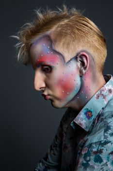 Portrait of beautiful young man with modern hairstyle, artistic multicolor makeup and rhinestones on the face. Studio shot. Black background