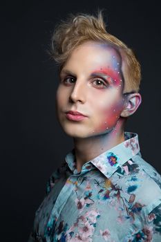 Portrait of beautiful young man with modern hairstyle, artistic multicolor makeup and rhinestones on the face. Studio shot. Black background