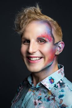 Portrait of beautiful young man with modern hairstyle, artistic multicolor makeup and rhinestones on the face. Studio shot. Black background