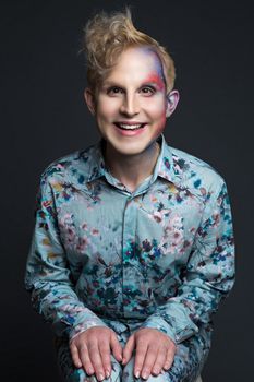 Portrait of beautiful young man with modern hairstyle, artistic multicolor makeup and rhinestones on the face. Studio shot. Black background