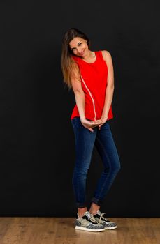 Beautiful young woman posing in front of a black wall with a shy expression