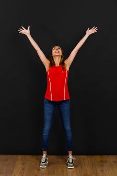 Beautiful happy woman with arms open in front of a black wall