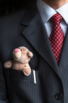 Close up with elegant stylish businessman keeping small teddy bear in his breast suit jacket pocket. Formal negotiations concept