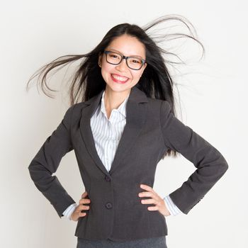 Portrait of Asian businesswoman in formalwear smiling and hands on waist, standing on plain background.