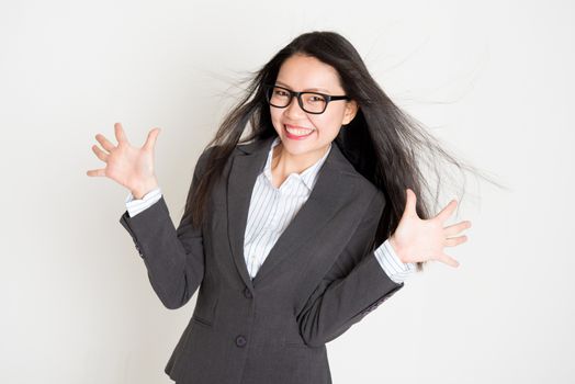 Portrait of happy Asian businesswoman in formalwear smiling and palms open, standing on plain background.