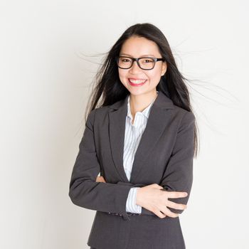 Portrait of young Asian businesswoman in formalwear smiling and looking at camera, standing on plain background.