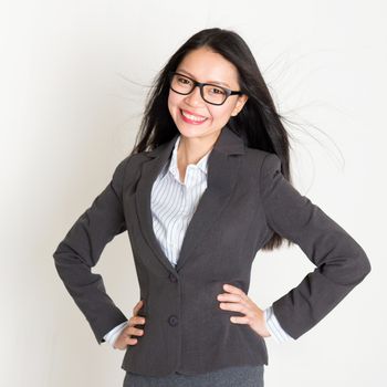 Portrait of young Asian business woman in formalwear smiling and looking at camera, standing on plain background.