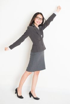 Portrait of happy Asian businesswoman in formalwear arm raised grabbing something and smiling, full body standing on plain background.