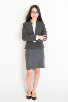 Portrait of young Asian businesswoman in formalwear smiling, full body standing on plain background.