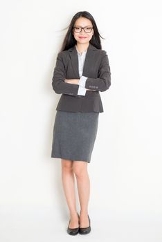 Portrait of Asian female businesswoman in formalwear smiling, full body standing on plain background.