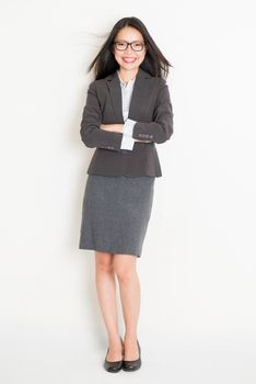 Portrait of Asian female business woman in formalwear smiling, full body standing on plain background.