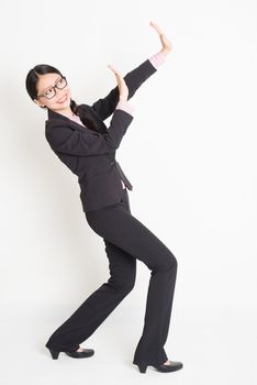 Full body portrait of young Asian businesswoman in formalwear hands defending on something, standing on plain background.