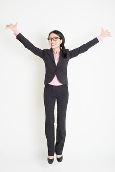 Full length front view of young Asian businesswoman in formalwear jumping in midair, on plain background.