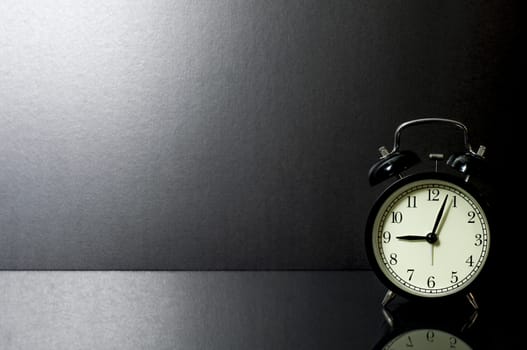 Still Life retro alarm clock on glass table in front of black background.