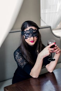 a beautiful girl sitting in the cafe with black mask and wine